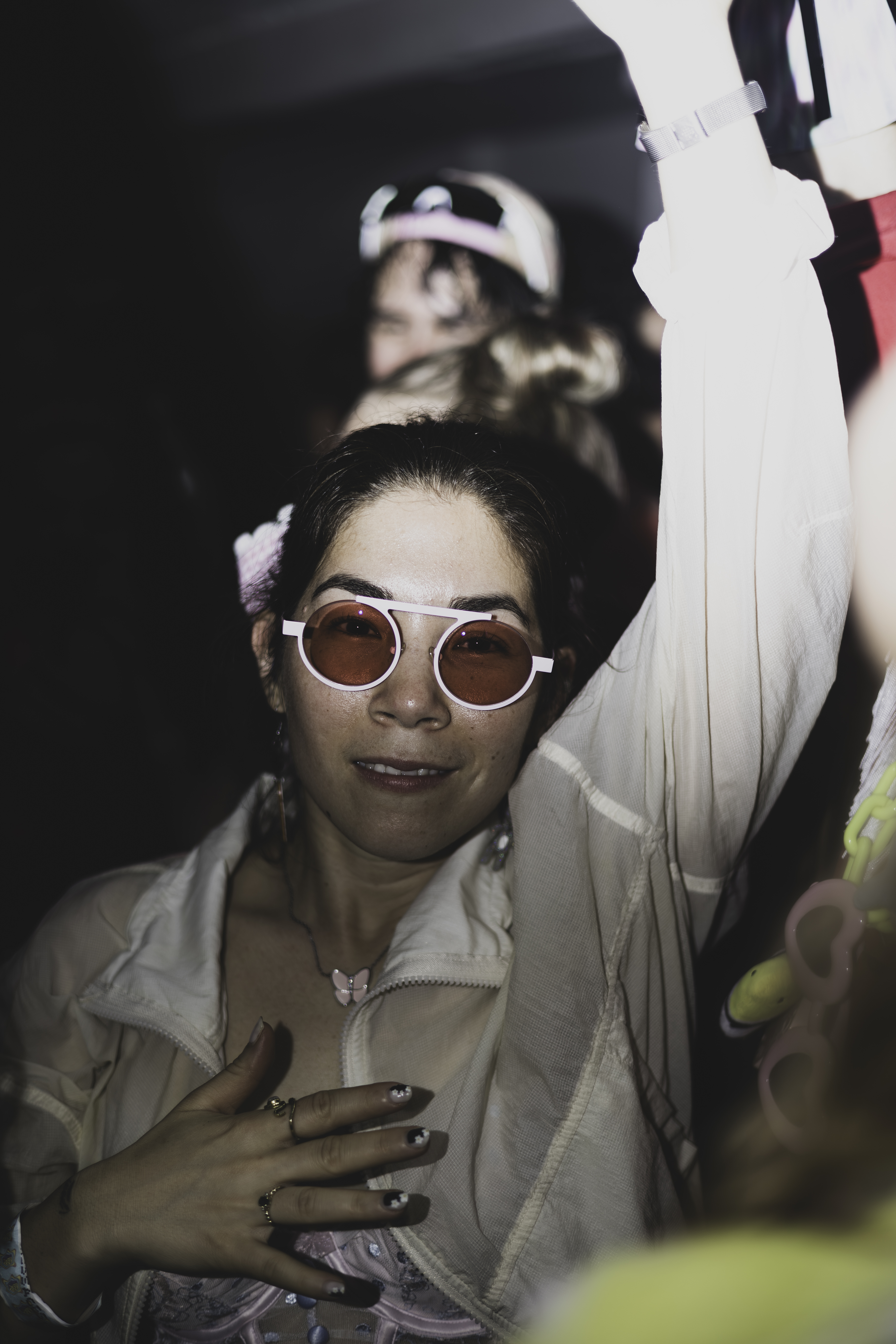 Woman with rose-tinted round sunglasses in a crowd, arm raised, nightlife
