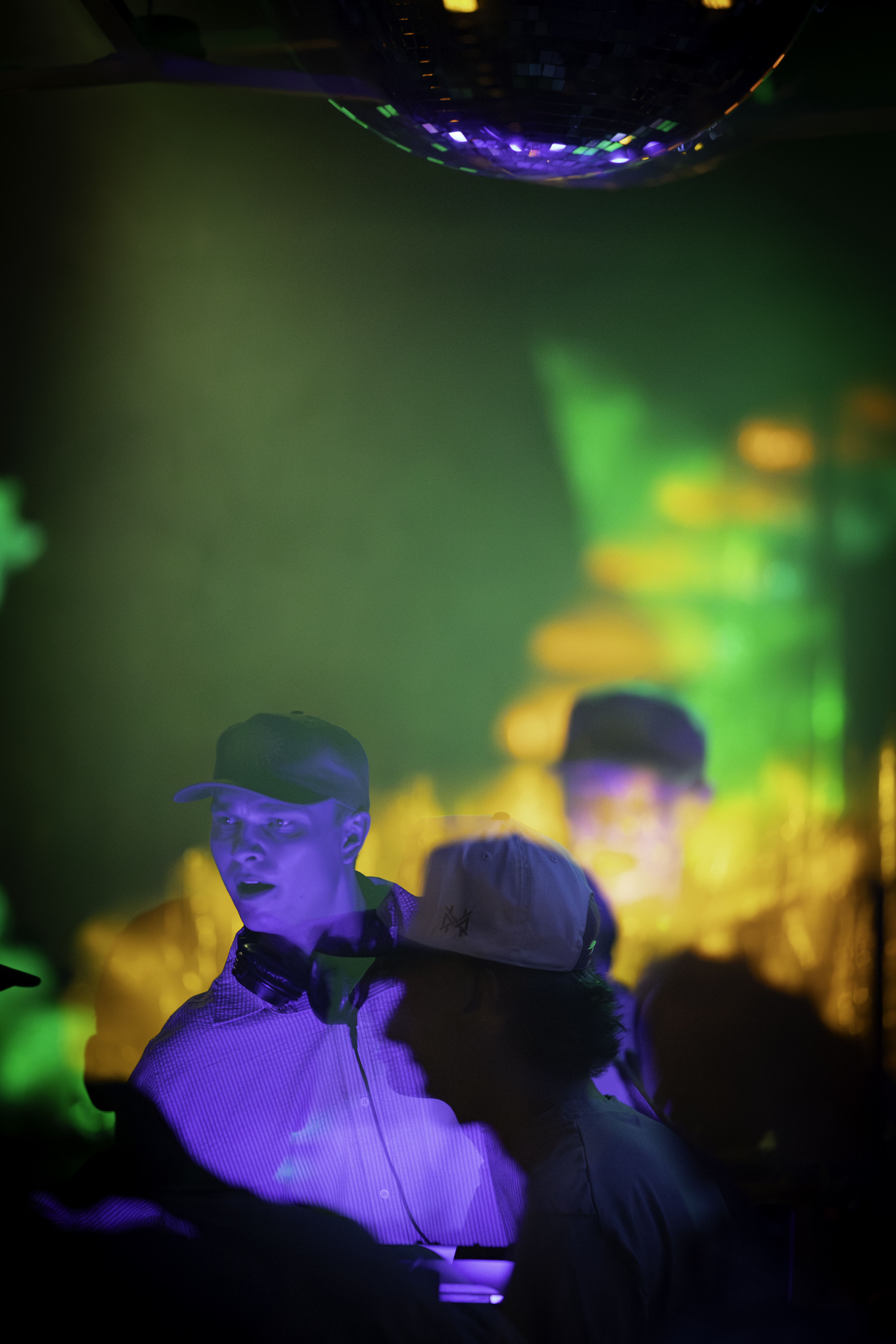 Two men under disco ball, green and purple club lighting