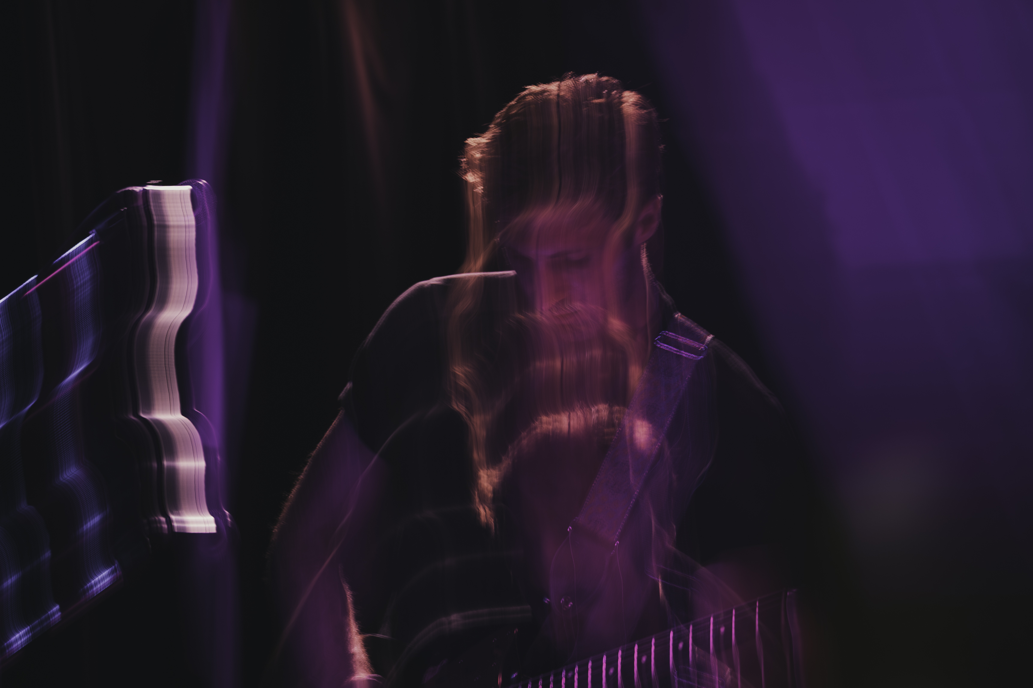 Long-exposure portrait of guitarist performing under purple stage lights