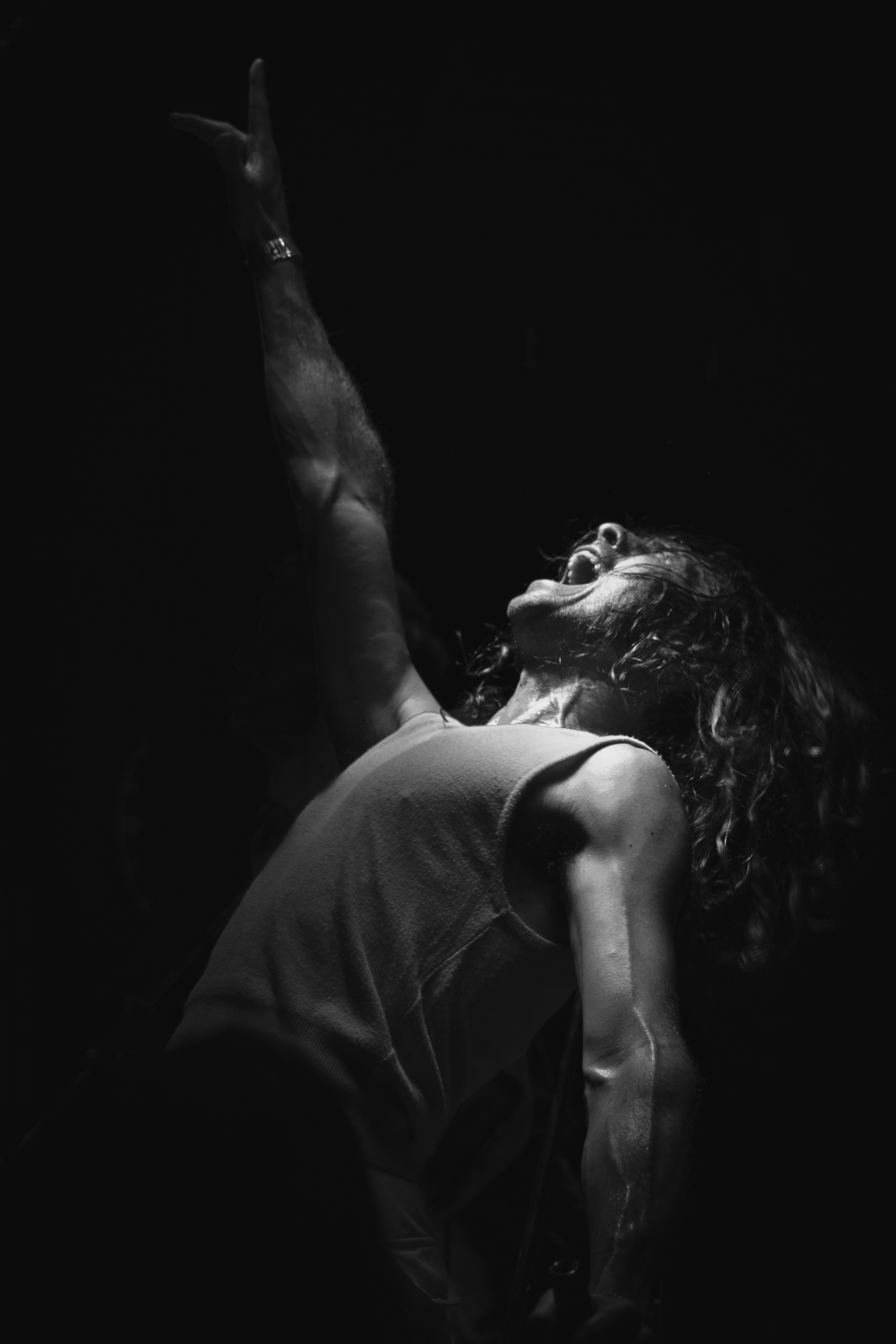 Black and white concert portrait, performer reaching arm upward against dark backdrop