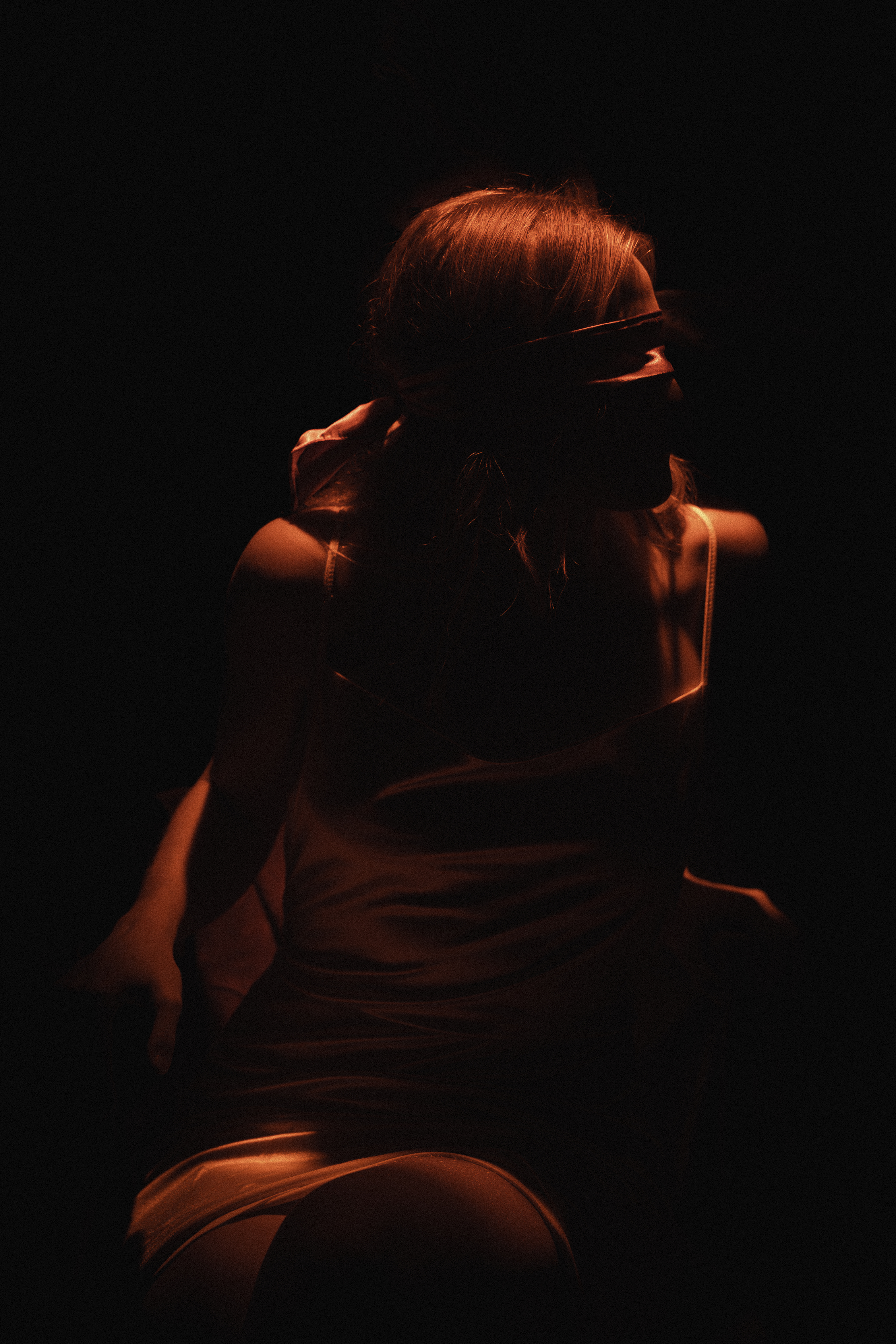 Woman from behind, warm amber light on hair and shoulders against black background